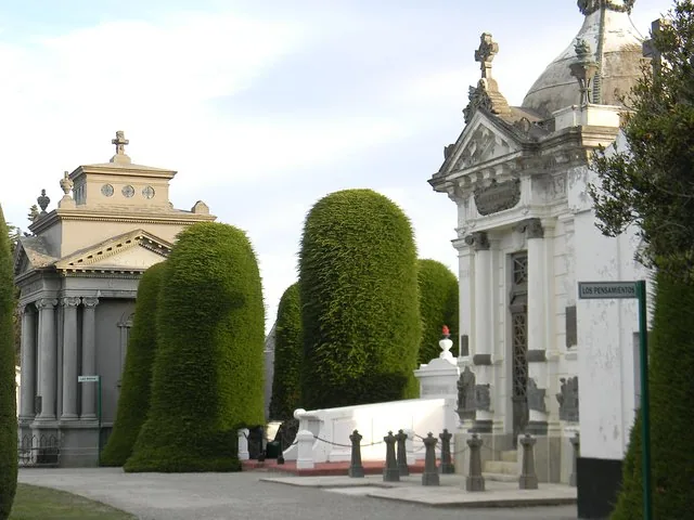 Ornate mausoleums and manicured conical evergreen trees in a cemetery